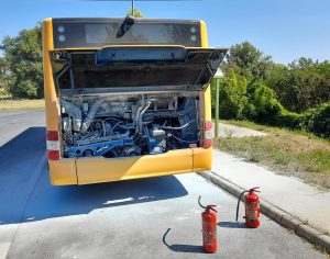 kiégett motorterű volánbusz áll egy megállóban, előtérben két poroltó készülékkel.